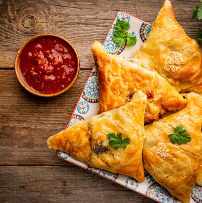 Samsa or samosas with meat and vegetables with tomato sauce on wooden background. Traditional asian food. Top view.